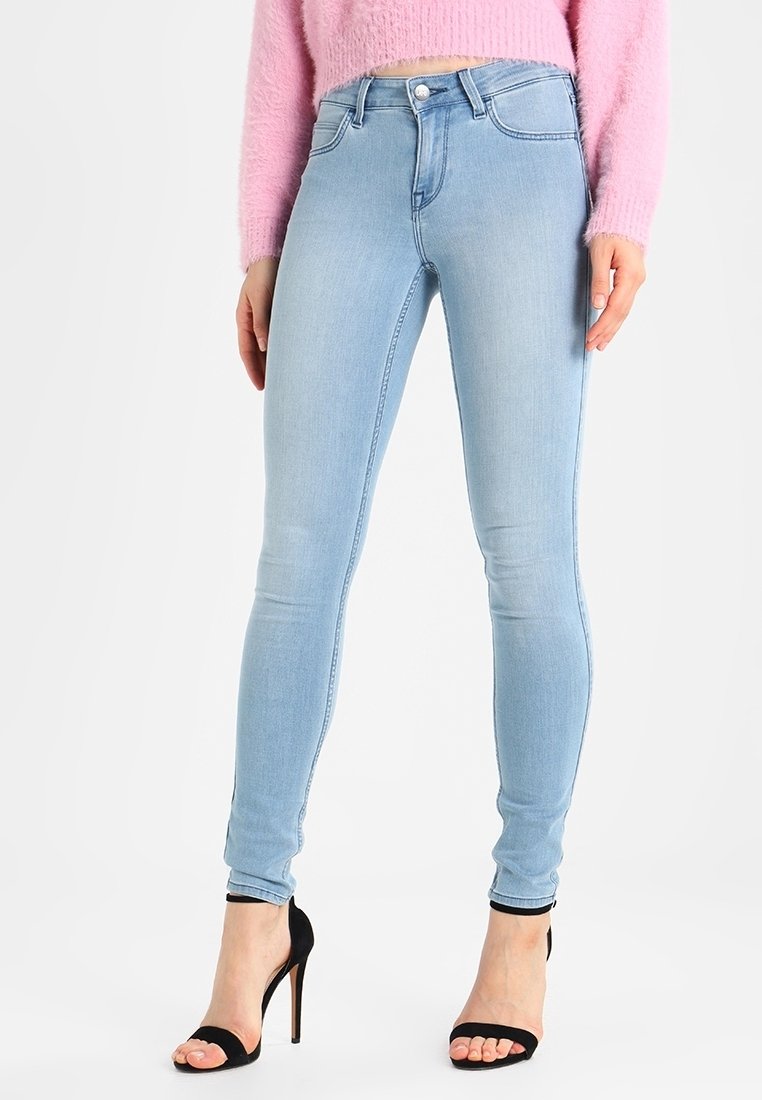 Jeans skinny azul claro de mezclilla, con cintura alta, cinco bolsillos y un cierre clásico de botón, combinados con tacones stiletto negros.