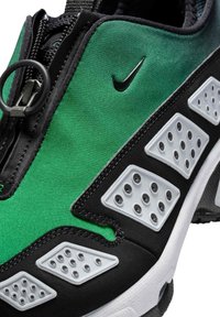 But sportowy Nike z zielonym materiałowym wierzchem, czarnymi akcentami oraz białą podeszwą z szarymi gumowymi nakładkami i perforowanymi detalami.