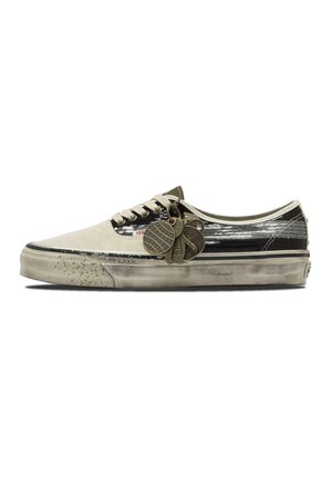 Scarpa bassa Vans con parte anteriore avorio, parte posteriore nera con paillettes argento, lacci bianchi, suola consumata e molteplici ciondoli metallici attaccati.