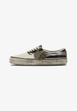 Scarpa bassa Vans con parte anteriore avorio, parte posteriore nera con paillettes argento, lacci bianchi, suola consumata e molteplici ciondoli metallici attaccati.