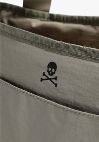 Bolso gris claro con un acento verde. Presenta un gráfico de calavera y huesos cruzados en el interior. Fabricado con un material suave y duradero.