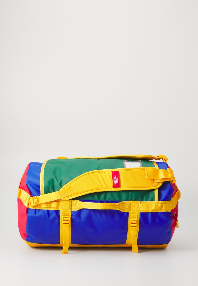 Colorful duffel bag featuring green, blue, red, and yellow sections, with yellow straps and buckles, and a small red logo tag.