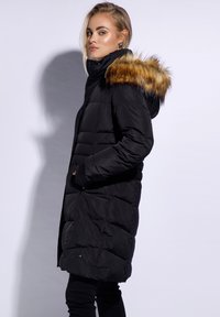Black puffer jacket with a fur-trimmed hood, featuring a quilted design, side pockets, and a mid-length cut. Smooth texture and modern appearance.