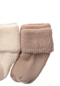 Zwei Paar Babystrümpfe in Creme und Beige, mit einem strukturierten umklappbaren Bündchen, weichem Stoff und einem leichten Strickdesign.