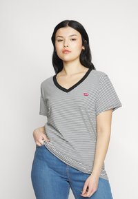 T-shirt a righe bianche e nere con scollatura a V e maniche corte, caratterizzato da un piccolo logo rosso Levi's sul petto. Abbinato a jeans blu.