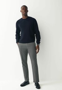 Mørkeblå sweater med ribstrikkede manchetter og rund hals, parret med grå skræddersyede bukser og sorte loafers, der har et elegant, minimalistisk design.