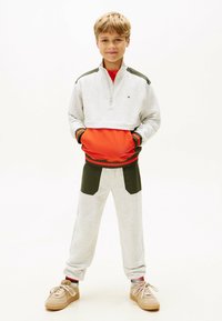Conjunto deportivo para niños que incluye una sudadera con cremallera en gris claro con detalles en naranja y verde oscuro, acompañada de pantalones jogger a juego.