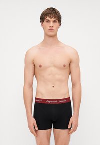 Culottes de boxeur noires avec une ceinture élastique bordeaux comportant du texte blanc. Tissu lisse, design ajusté et longueur mi-cuisse.