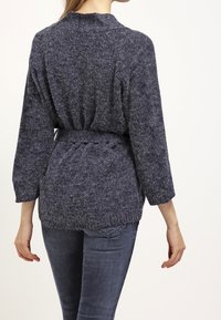 Marinblå stickad cardigan med avslappnad passform, bälte i midjan och trekvartslånga ärmar. Mjuk struktur och subtilt mönster synligt.