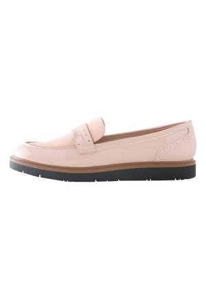 Person iført lyseblå opkørte jeans og pink læder loafers, der står på en grå gulv.