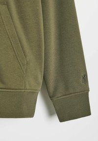 Oliwkowy sweter z kieszenią kangurzą, ściągaczami w mankietach i małym haftowanym logo na rękawie. Miękka tekstura materiału.