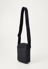 Svart axelväska i mjukt material, med rektangulär form, justerbar rem och minimalistisk design med dragkedja.