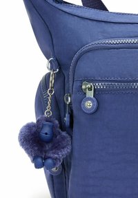 Marinblå tygryggsäck med en strukturerad utsida, flera zippered fack och en fluffig apnyckelring som accent.