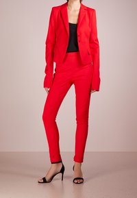 Červený přizpůsobený blejzr a odpovídající slim-fit kalhoty vyrobené z hladkého materiálu. Dlouhé rukávy, klopové límce a štíhlý silueta. Černé sandály na podpatku.