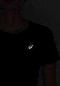 Svart t-shirt med en reflekterande logga på vänster bröstområde. Tyget verkar slätt, med en klassisk rund halsdesign.