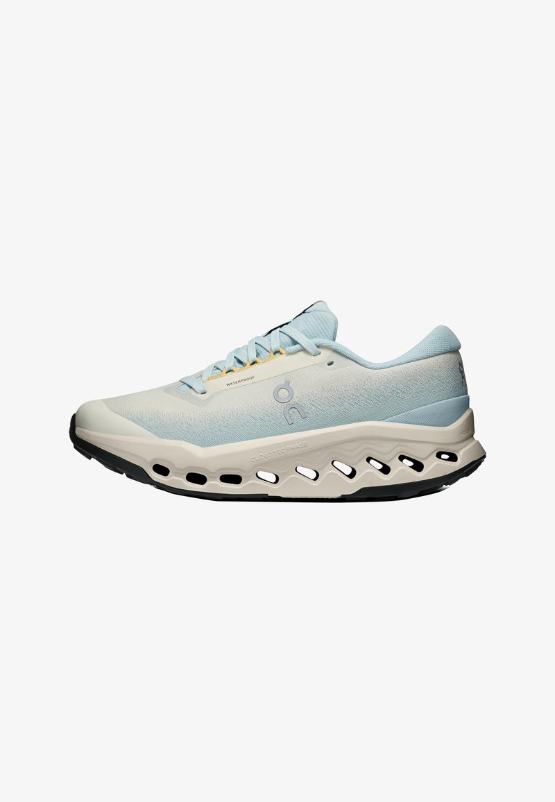 Chaussure de course bleu clair et beige avec fermeture à lacets, semelle rembourrée perforée et étiquette imperméable sur le côté.