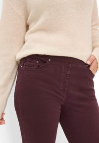 Bordeaux bukser med en glat tekstur og elastisk talje, udstyret med to forlommer, metalhardware og kontrasterende syninger.