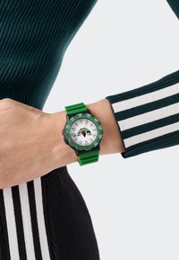 Roheline silikoonist kell, millel on valge taust, mustad aktsendid ja punased detailid; suured numbrid ning tekstuuriga rihm, mis tagab hea haarde.