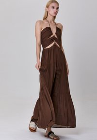 Robe maxi halter marron avec un corsage froncé, des découpes à la taille et une jupe à volants. Tissu léger et fluide avec une texture lisse.