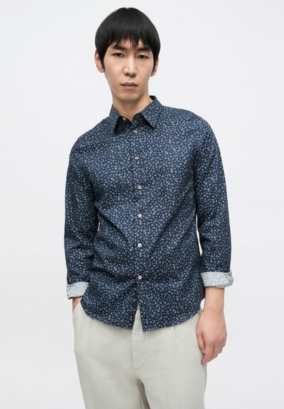 Σκούρο μπλε πουκάμισο με κουμπιά και μικρό ανοιχτό μπλε λουλουδένιο μοτίβο, μακριά μανίκια φουσκωμένα μέχρι τον καρπό, μαλακό ύφασμα και διακριτική λεπτομέρεια γιακά.