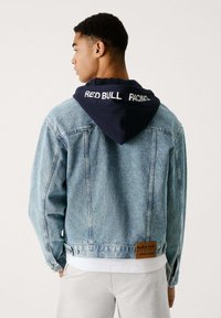 Leren spijkerjack in lichtblauw met een marineblauwe capuchon met de tekst "RED BULL RACING". Inclusief een logo patch op de achterzoom en een verouderde structuur.