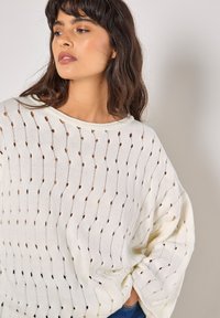 Leichtes Cremefarbenes Pullover mit entspannter Passform. Verfügt über ein offenes Strickmuster mit abwechselnden runden und diamantförmigen Designs. Weiche Textur, runder Ausschnitt.