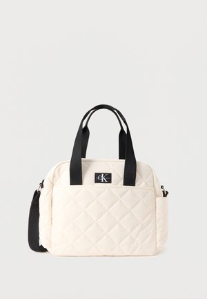 Sac à main matelassé crème avec poignées noires, poche avant, poche latérale, et patch avec logo Calvin Klein.
