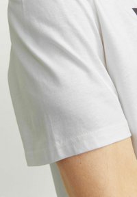 Weißes Baumwoll-T-Shirt mit Rundhalsausschnitt und kurzen Ärmeln. Der Stoff wirkt glatt, mit Nähten an den Ärmeln und am Saum.