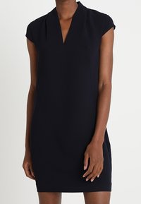 Sleeveless black dress with a V-neckline worn by a person standing against a plain background.