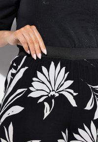 Černá tkanina s bílým květinovým vzorem; obsahuje černý elastický pas a texturovaný černý vršek se dekorativními prvky.