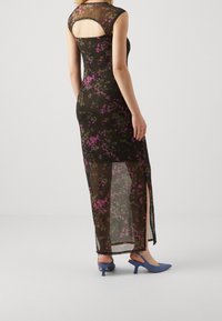 Schwarzes Maxikleid mit kurzen Ärmeln und ausgeschnittenem Rücken. Der Stoff ist durchsichtig und hat lila und grüne Muster. Kombiniert mit blauen High Heels.