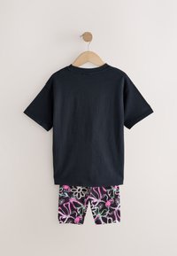 Tricou bleumarin din bumbac, cu mâneci scurte și guler rotund, asortat cu pantaloni scurți negri având un model floral colorat în roz și alb.