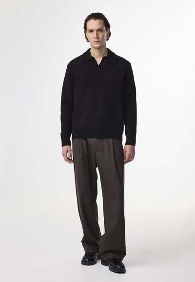 Maglione nero a maglia con colletto largo, abbinato a pantaloni marroni larghi e scarpe nere con dettagli testurizzati.