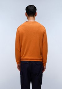 Maglione lavorato a maglia arancione con maniche lunghe e colletto rotondo, abbinato a pantaloni cargo blu scuro con tasche laterali e dettagli con bottoni.