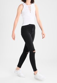 Vit ribbad linne med snörning framtill, i kombination med svarta skinny jeans med slitna knän och fransiga fållar, avslutat med vita sneakers.