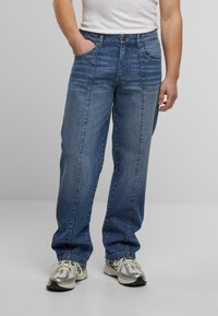 Lys blå denimjeans, løs passform, to frontlommer, falmet tekstur, midje med knappelukking, brukt med grå sneakers.