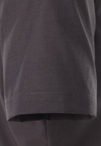 Donkergrijze stoffen kleding met een opgevouwen mouw. Het materiaal lijkt glad met een subtiele textuur en nette stiksels langs de zoom.