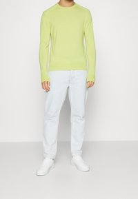 Pull en maille vert clair à manches longues et à encolure ronde, assorti à un jean bleu clair et des baskets blanches. Design simple, sans motifs.