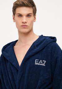 Tamsiai mėlynas frotė chalatas su gobtuvu, su krūtinės logotipu "EA7 Emporio Armani", išsiskiriantis minkšta tekstūra ir laisvu dizainu.