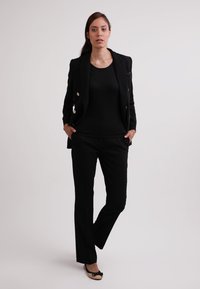 Completo da lavoro nero con blazer su misura caratterizzato da bottoni in argento, abbinato a pantaloni neri attillati e ballerine nere con dettaglio a fiocco.