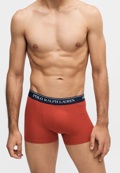 Άνδρας κορμός που φοράει κόκκινα boxer briefs με μπλε ναυτικό ζωνάρι μέσης με λευκή σήμανση "Polo Ralph Lauren".
