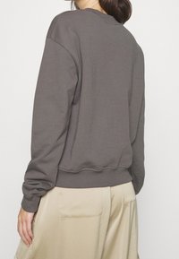 Grå bomullströja med rundad nacke, ribbade muddar och nederkant, med en avslappnad passform och mjuk textur. Bakvy visar en enkel design.