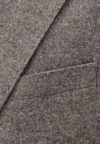 Grauer Wollblazerstoff mit dezenter Textur und einer Paspeltasche auf der linken Seite, die das maßgeschneiderte Design betont.