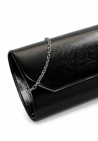 Sac à main en cuir verni noir avec une surface texturée, doté d'une chaîne en métal argenté et d'une fermeture à rabat aux bords angulaires.