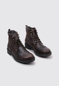 Bottines en cuir marron avec une finition texturée, bout rond et coutures contrastantes. Présente des œillets en métal et une doublure intérieure à motif.