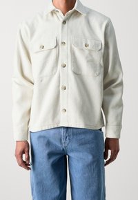 Witte textuur-overhemd met twee borstzakken, parelgekleurde knopen en een relaxed fit, gecombineerd met lichtblauwe denim jeans.