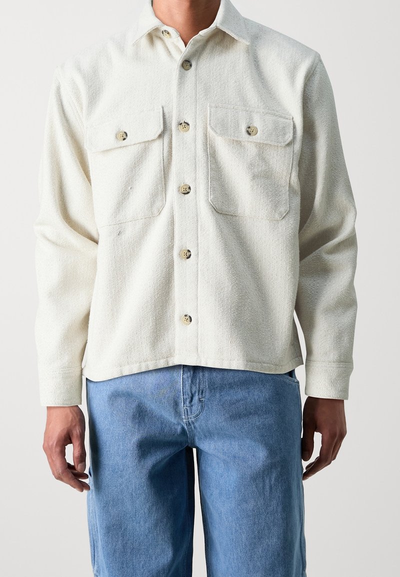 Witte textuur-overhemd met twee borstzakken, parelgekleurde knopen en een relaxed fit, gecombineerd met lichtblauwe denim jeans.