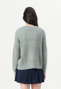 Lys grønn strikkegenser med et strukturert mønster, lange ermer og rund hals, kombinert med et marineblått plisserte skjørt.
