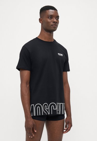 T-shirt en coton noir arborant une inscription « MOSCHINO » en lettres blanches audacieuses sur le bas du devant, col rond et manches courtes. Texture lisse.