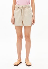 Beige denim shorts with a drawstring waist, featuring front pockets and a relaxed fit. Paired with clear strappy sandals.